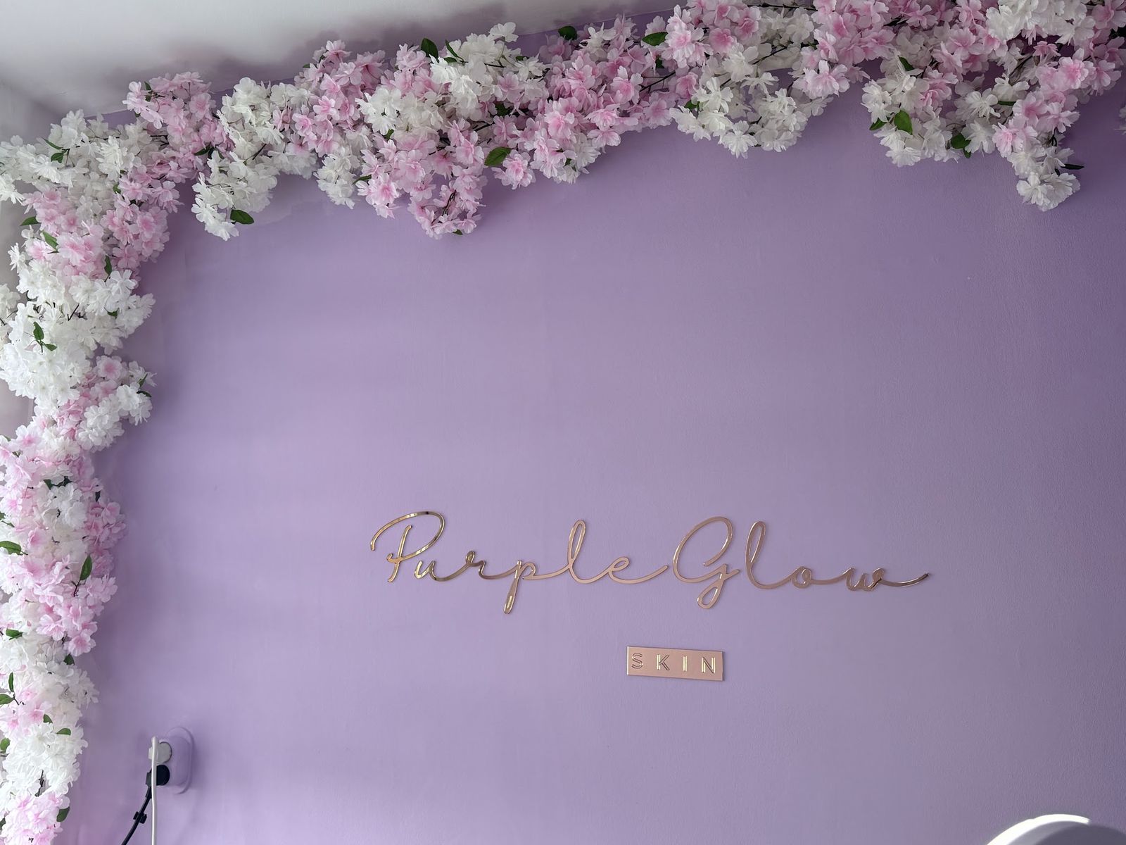 De lila wand met bloesem en de rosé-gouden letters PurpleGlow Skin