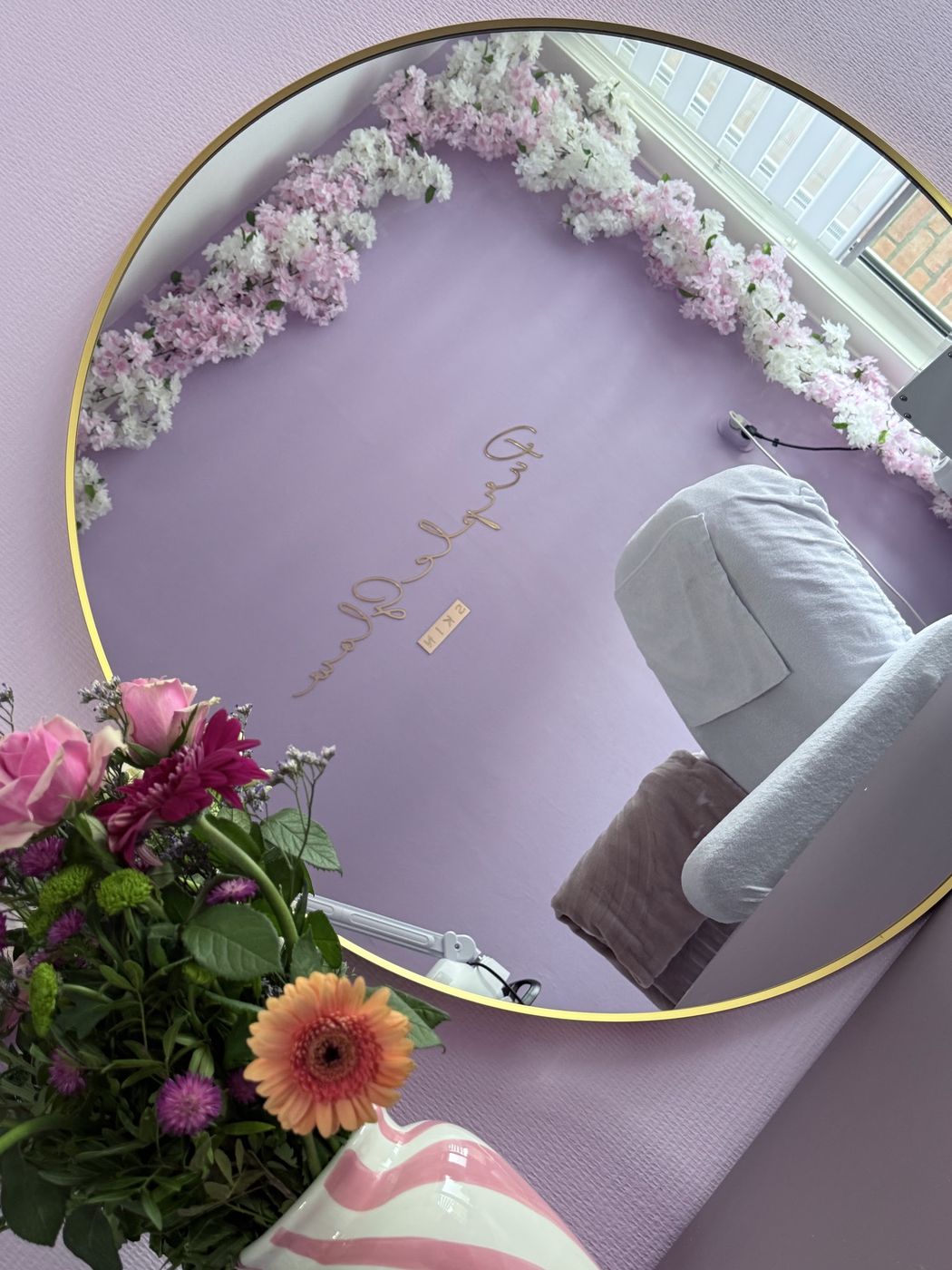 De behandelstoel met witte handdoek, gezien in de ronde spiegel, met een boeket bloemen ervoor